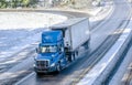 Big rig blue day cab semi truck transporting cargo in reefer semi trailer driving on winter wet road with snow Royalty Free Stock Photo