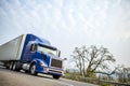 Big rig blue modern semi truck with dry van semi trailer driving on the road with safety fence Royalty Free Stock Photo