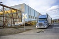 Big rig blue semi truck with grille guard standing with open semi trailer on the road shoulder in industrial area waiting for next Royalty Free Stock Photo