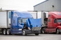 Big rig blue semi truck with open hood standing on the parking lot waiting for engine inspection and maintenance