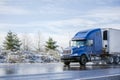 Big rig blue semi truck tractor transporting commercial cargo in refrigerator semi trailer going on the wet road with melting snow Royalty Free Stock Photo