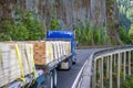 Big rig blue semi truck with two flat bed semi trailers transporting lumber running on the bridge on the road around of the Royalty Free Stock Photo