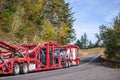 Big rig car hauler semi truck transporting cars on red two level semi trailer running on winding autumn road