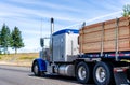 Big rig classic blue bonnet semi truck tractor transporting lumber wood on flat bed semi trailer on the road with hill on the side Royalty Free Stock Photo