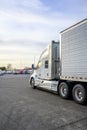 Big rig classic bonnet semi truck with refrigerator semi trailer running on the truck stop parking lot past other parked trucks