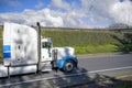 Big rig classic industrial transportation semi truck with chrome exhaust pipes and high cab running on the local road with hill on