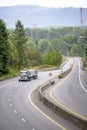 Big rig tip truck with two semi trailers driving on winding divided highway road with forest on the sides Royalty Free Stock Photo