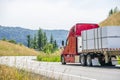 Big rig classic red semi truck transporting covered and tightened by straps cargo on flat bed semi trailer truveling in Columbia Royalty Free Stock Photo