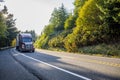 Big rig dark red semi truck with grille guard transporting frozen food in refrigerator semi trailer running on the road with trees Royalty Free Stock Photo