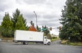 Big rig day cab semi truck with long box trailer turning on freeway entrance from local road with traffic lights and trees Royalty Free Stock Photo