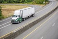 Big rig day cab semi truck with roof spoiler transporting dry van semi trailer running on the turning divided highway road with