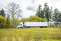 Big rig day cab semi truck transporting frozen cargo in refrigerator semi trailer running on the road on the hill with trees on Royalty Free Stock Photo