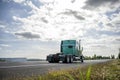 Green classic big rig semi truck tractor driving on the road with cloudy sky to warehouse for pick up the loaded trailer Royalty Free Stock Photo