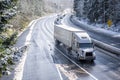 Big rig semi truck with semi trailer driving on winter snowy highway with wet melting snow surface