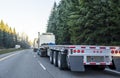 Big rig long haul semi truck with empty flat bed semi trailer running on the winter road in convoy with another semi trucks