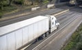 Dirty after rain big rig semi truck with dry van semi trailer running on the wide multilines highway road with trees on the hill Royalty Free Stock Photo