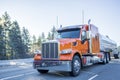 Big rig orange classic American semi truck transporting liquid cargo in tank semi trailer moving on the winter frosty road