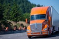 Big rig orange semi truck and trailer running on green highway w