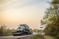 Big rig semi truck transporting oversized tip truck on step down semi trailer on winding evening road Royalty Free Stock Photo