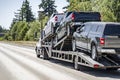 Big rig powerful car hauler semi truck transporting pick up trucks on the modular semi trailer driving on the multiline highway