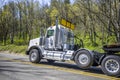 Big rig powerful semi truck tractor with oversize load sign on the roof transporting cargo on step down heavy-duty semi trailer