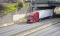 Big rig red bonnet long haul semi truck transporting cargo in dry van semi trailer running under the bridge over the wide divided Royalty Free Stock Photo