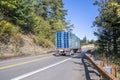 Big rig red semi truck transporting stacked wooden pallets on the flat bed semi trailer running on the winding narrow road Royalty Free Stock Photo