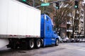 Big rig semi truck in blue with trailer moving by urban city street with modern building and cars Royalty Free Stock Photo