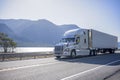 Big rig semi truck with chrome accessories transporting frozen cargo in refrigerated semi trailer moving on the road along river Royalty Free Stock Photo