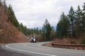 Big rig semi truck with conveyor belt mechanism driving by winding road with forest hills