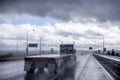 Big rig semi truck with empty flat bed semi trailer going on the raining highway with with rain dust spray