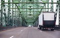 Big rig semi truck with lifting back door unit going highway along truss bridge Royalty Free Stock Photo