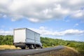 Big rig semi truck with long box trailer driving on the winding road with forest and meadow Royalty Free Stock Photo