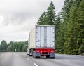 Big rig semi truck transporting cargo in long container mounted on a flat bed semi trailer running on the wide road with green Royalty Free Stock Photo