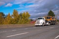 Big rig semi truck transporting equipment on step down semi trailer moving on wide autumn highway Royalty Free Stock Photo