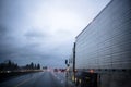 Big rig semi truck transporting frozen cargo in refrigerator semi trailer driving on the raining night highway with reflection