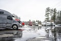 Big rig semi trucks with different semi trailers standing in row on the half empty winter truck stop parking lot with snow and Royalty Free Stock Photo