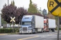 Big rig semi trucks with grille guard and reefer semi trailer standing on a railway crossing road in an industrial zone waiting Royalty Free Stock Photo