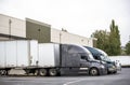 Big rig semi trucks with semi trailers standing in the warehouse dock loading cargo for next delivery Royalty Free Stock Photo