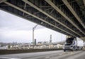 Big rig stylish black semi truck with semi trailer transporting cargo running on the lower level of two levels long bridge across Royalty Free Stock Photo