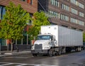 Big rig white day cab semi truck for local delivery transporting cargo in dry van semi trailer driving on the city street Royalty Free Stock Photo