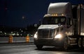 Big rig white day cab semi truck transporting cargo in semi truck driving on the wet rainy road in dark night time