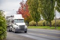 Big rig white day cab semi truck transporting liquid cargo in tank semi trailer running on autumn city road Royalty Free Stock Photo