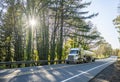 Big rig white day cab semi truck transporting liquid cargo in tank semi trailer running on the forest autumn road Royalty Free Stock Photo