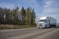 Big rig white industrial grade professional semi truck transporting cargo in dry van semi trailer moving on the multiline highway Royalty Free Stock Photo