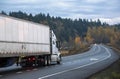 Big rig white long haul semi truck with semi trailer running on the winding evning road with trees and hills Royalty Free Stock Photo