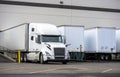 Big rig white semi truck with dry van semi trailer loading cargo in warehouse dock beside another semi trailers Royalty Free Stock Photo