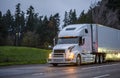 Big rig white semi truck with grille guard transporting cargo in dry van semi trailer running on the evening road with turned on Royalty Free Stock Photo