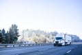 Big rig white semi truck with refrigerator semi trailer driving on the winter highway with snow and frozen trees on the hillside