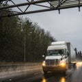 Big rig white semi truck with semi trailer driving on wet raining evening road with turned on headlight and reflection Royalty Free Stock Photo